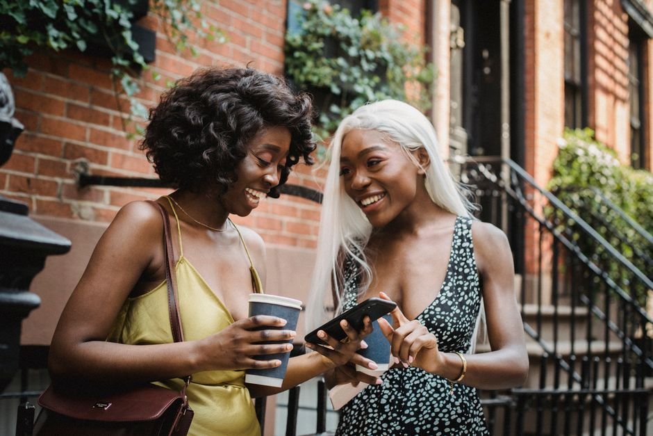 Deux amies riant en consultant un bon plan de parrainage sur leur téléphone, dans la rue
