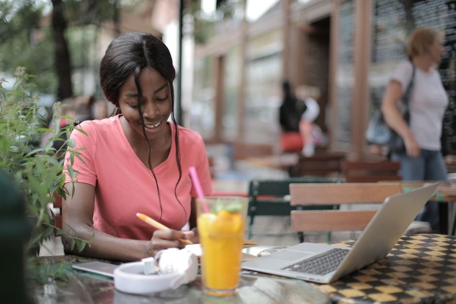 Femme souriante qui compare des offres sur son ordinateur portable en terrasse